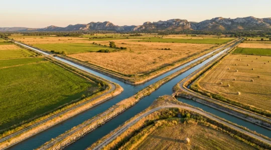 Vue aérienne des canaux d'irrigation traversant les prairies verdoyantes de la plaine de la Crau avec les Alpilles en arrière-plan